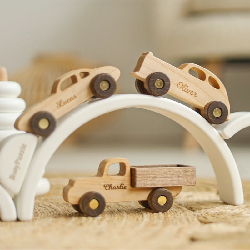 Natural wood toy cars on a white play arch, including a pick-up truck engraved with a name