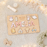 Wooden name board with decorative letters spelling 'AMELIA' on a soft surface with lights and flowers.