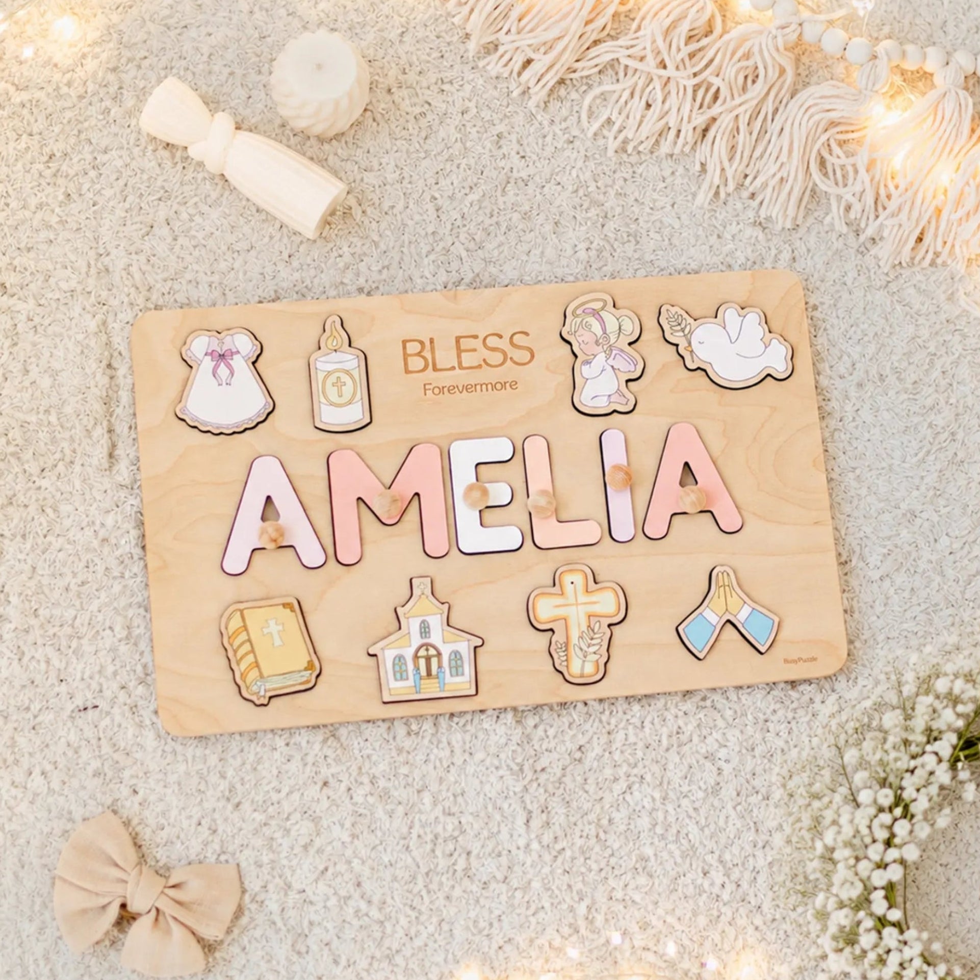 Wooden name board with decorative letters spelling 'AMELIA' on a soft surface with lights and flowers.