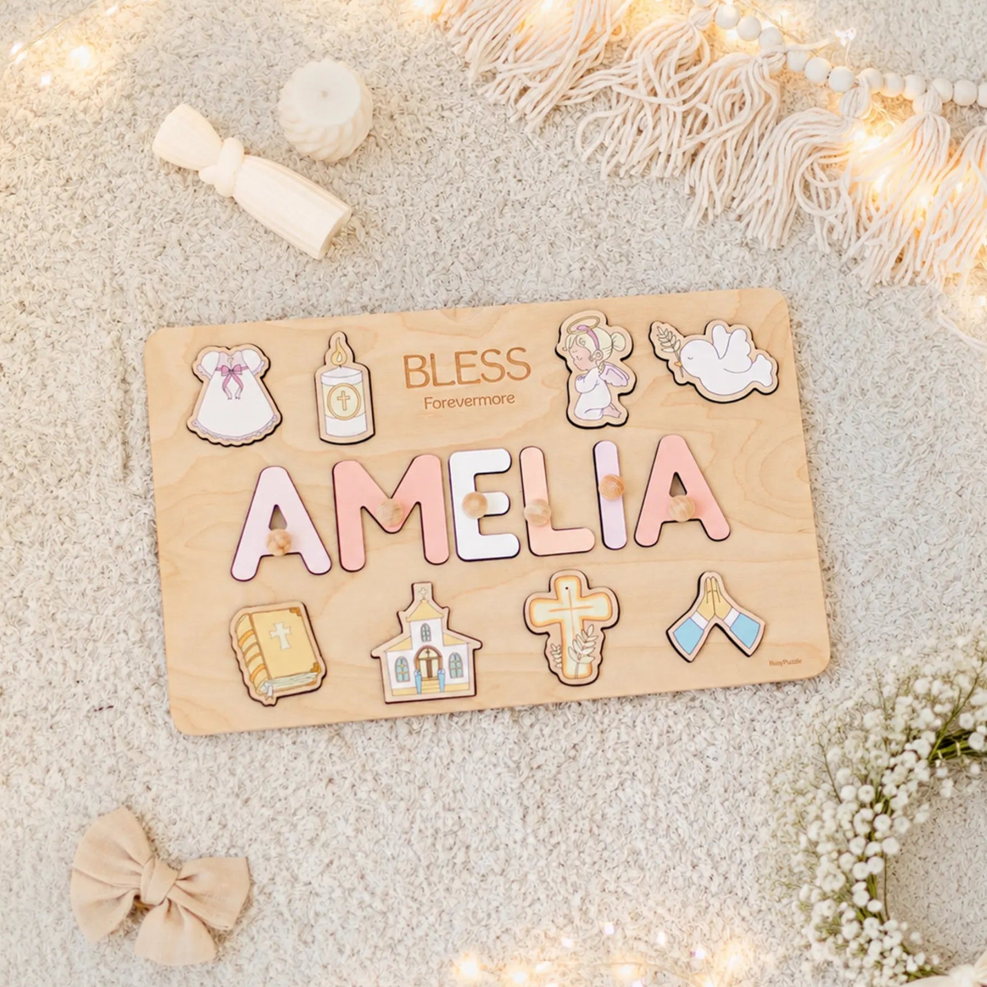 Wooden name board with decorative letters spelling 'AMELIA' on a soft surface with lights and flowers.