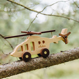 Wooden helicopter toy with engraved name, placed on a tree branch with a blurred natural background.