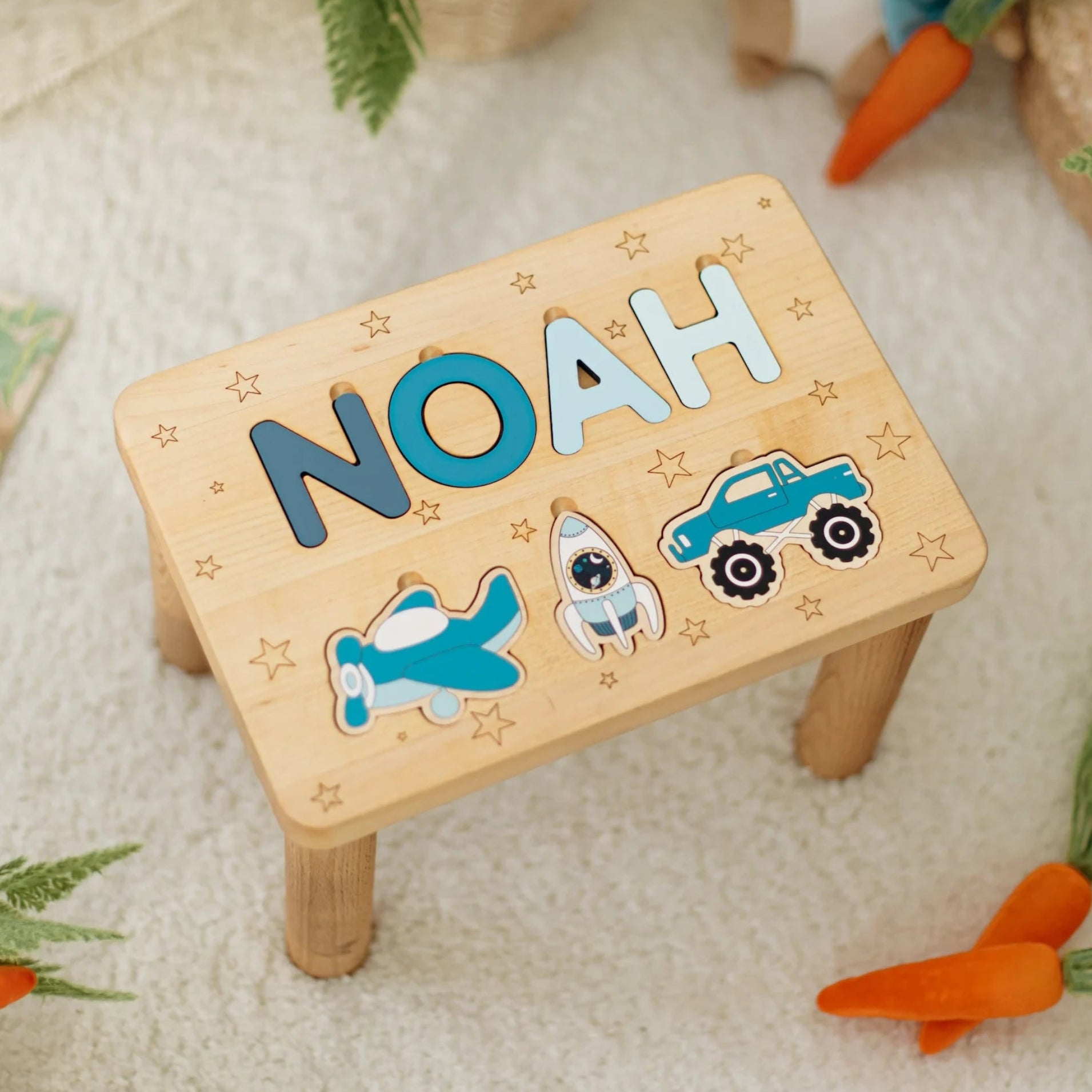Wooden step stool with 'NOAH' and vehicle elements on a soft surface.