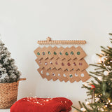 Wooden advent calendar mounted on a wall with kraft envelopes hanging from hooks beside a Christmas tree