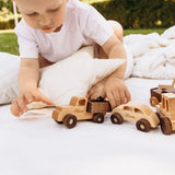 Toddler playing with natural wood toy cars on white bedding outdoors