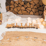 Wooden train decoration with 'Liam' on a textured surface with logs in the background