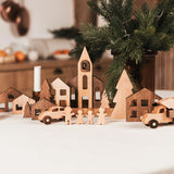 Wooden Christmas village scene with houses, cars, and trees on a white surface.