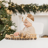 Child playing with a wooden train set in a festive setting with Christmas decorations.