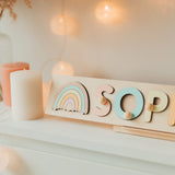 Wooden name puzzle with rainbow design on a shelf with candles and decorative lights.