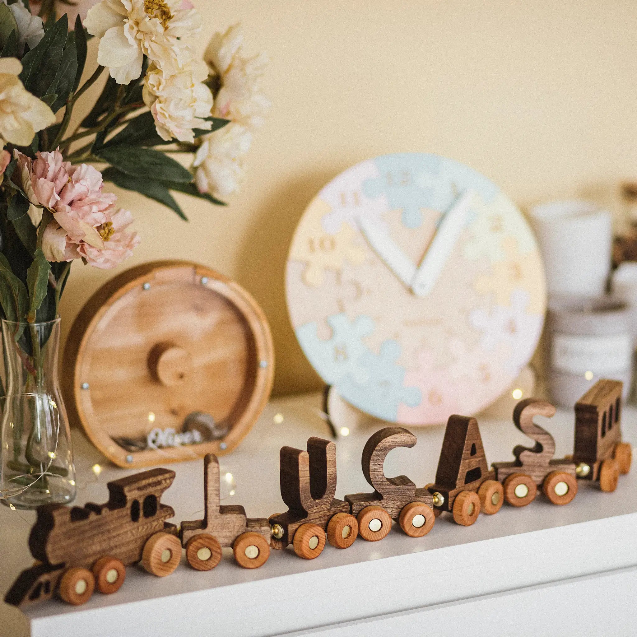 Wooden train name decoration with 'LUCAS' on a shelf with flowers and decor items.