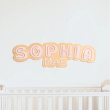 Decorative name sign 'SOPHIA MAE' above a crib on a light blue wall.