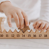 Child's hand moving the wooden star on a light wood advent calendar, days 10 to 18