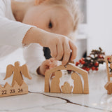Toddler placing a wooden Nativity arch on an advent calendar base with an angel figurine
