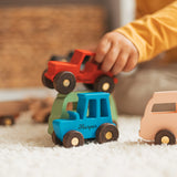 Child reaching for red and blue wooden toy cars on a woven basket