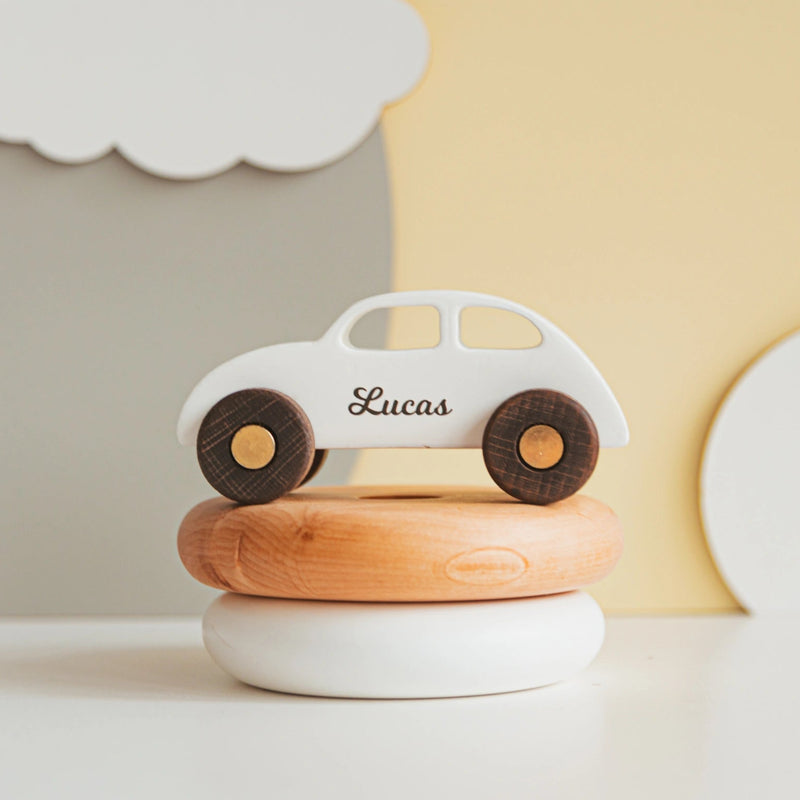 Personalized white wooden coupe car with the name Lucas, resting on a wooden stacking-ring toy in a nursery