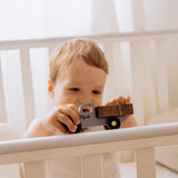 Child holding a toy truck with engraved name on it in a crib.