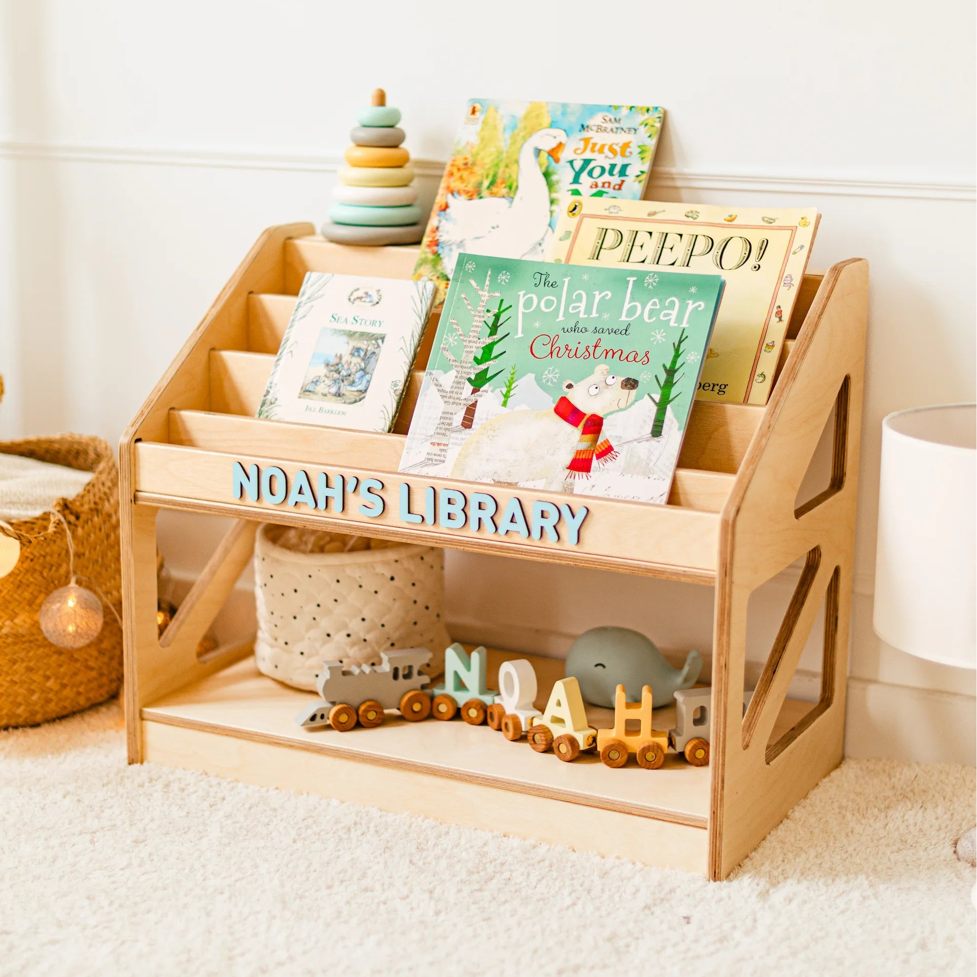 Light wood personalized Montessori bookshelf named Noah's Library filled with children's picture books in a bright nursery