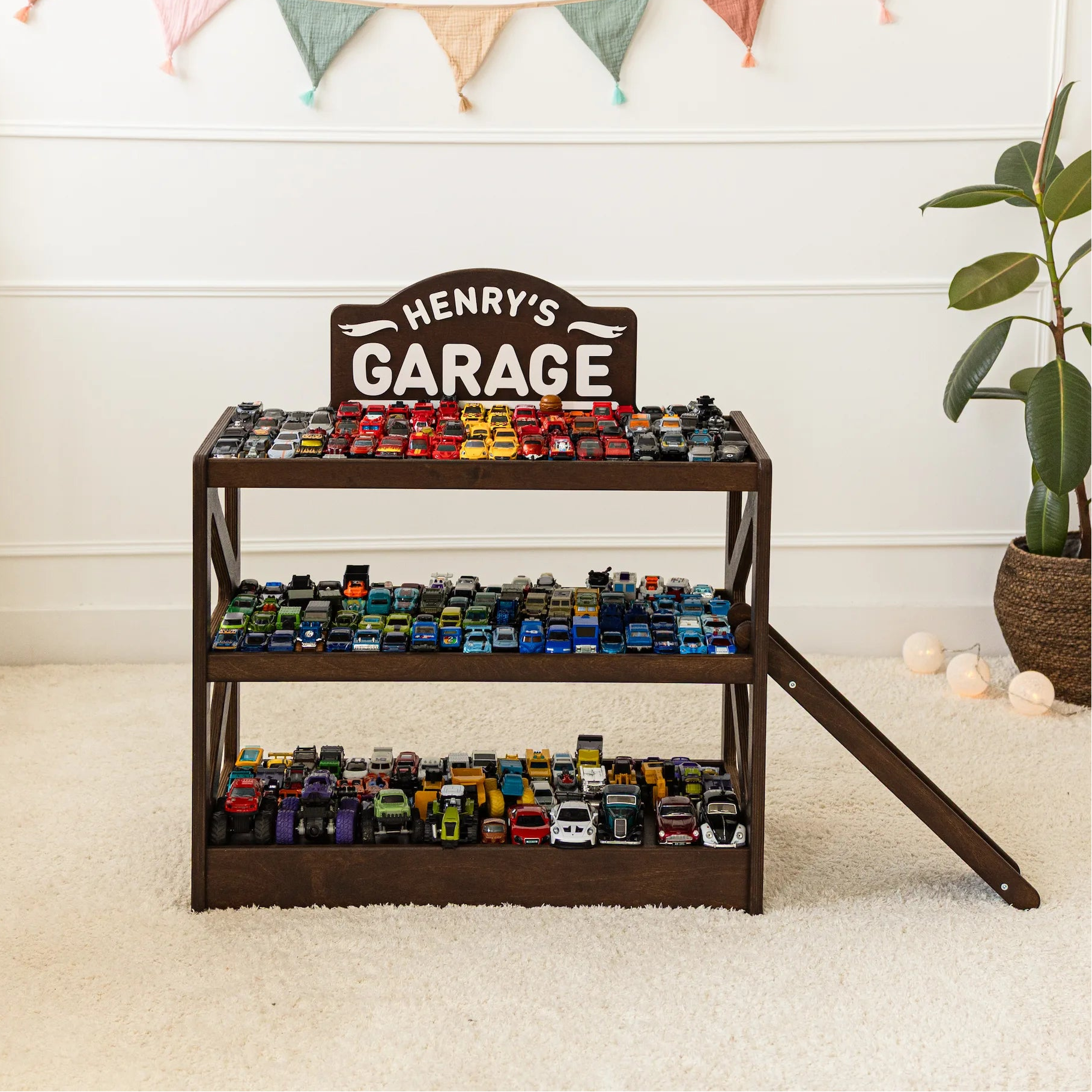 Dark wood personalized toy car garage named Henry's Garage, three tiers filled with toy cars and a ramp in a nursery