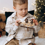 Child holding a wooden toy car in front of a decorated Christmas tree