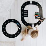 Child playing with a road track set on a light wooden floor