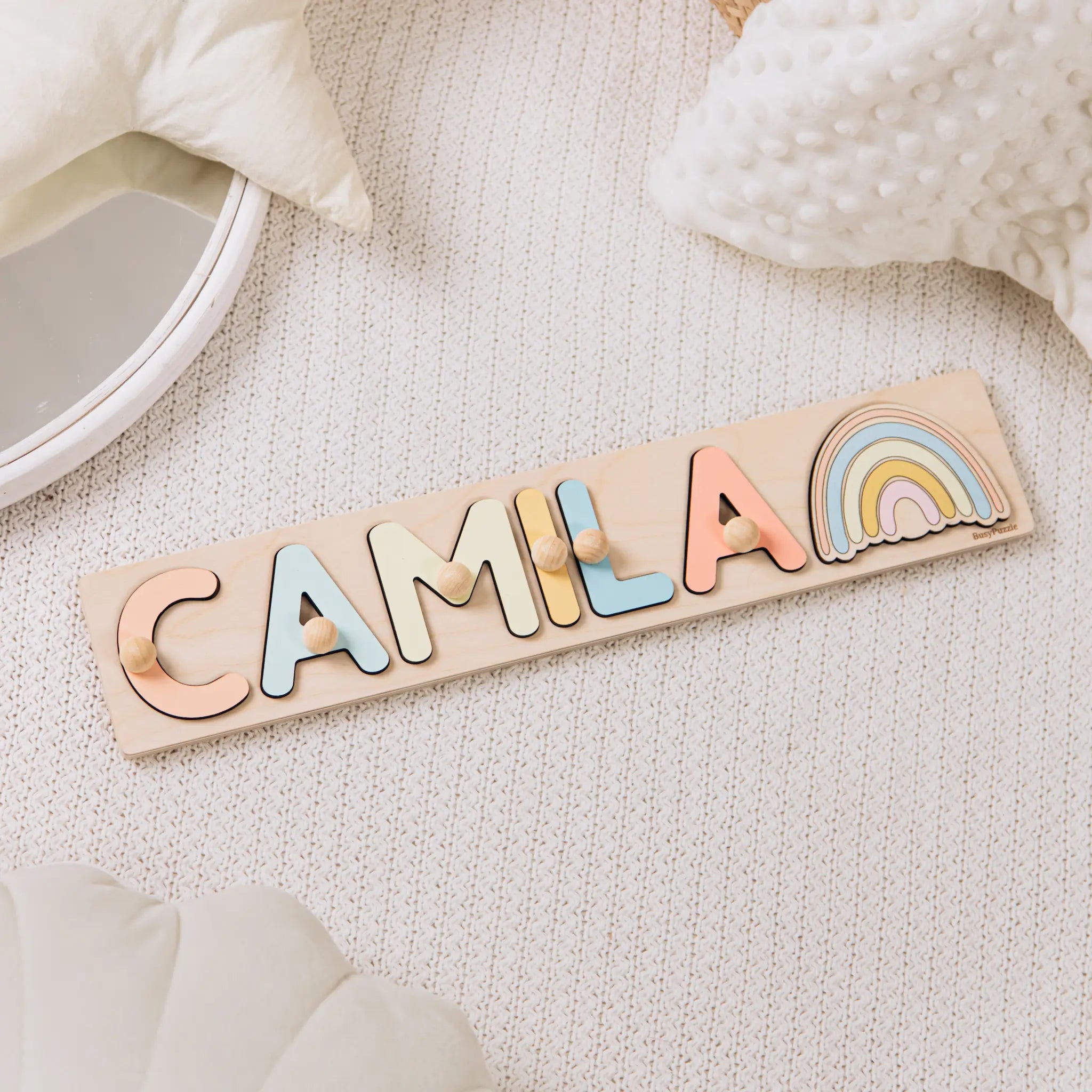 Wooden name puzzle with colorful letters spelling 'Camila' on a soft surface.