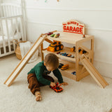 Toddler playing on the floor beside a light wood toy car garage named Oliver's Garage