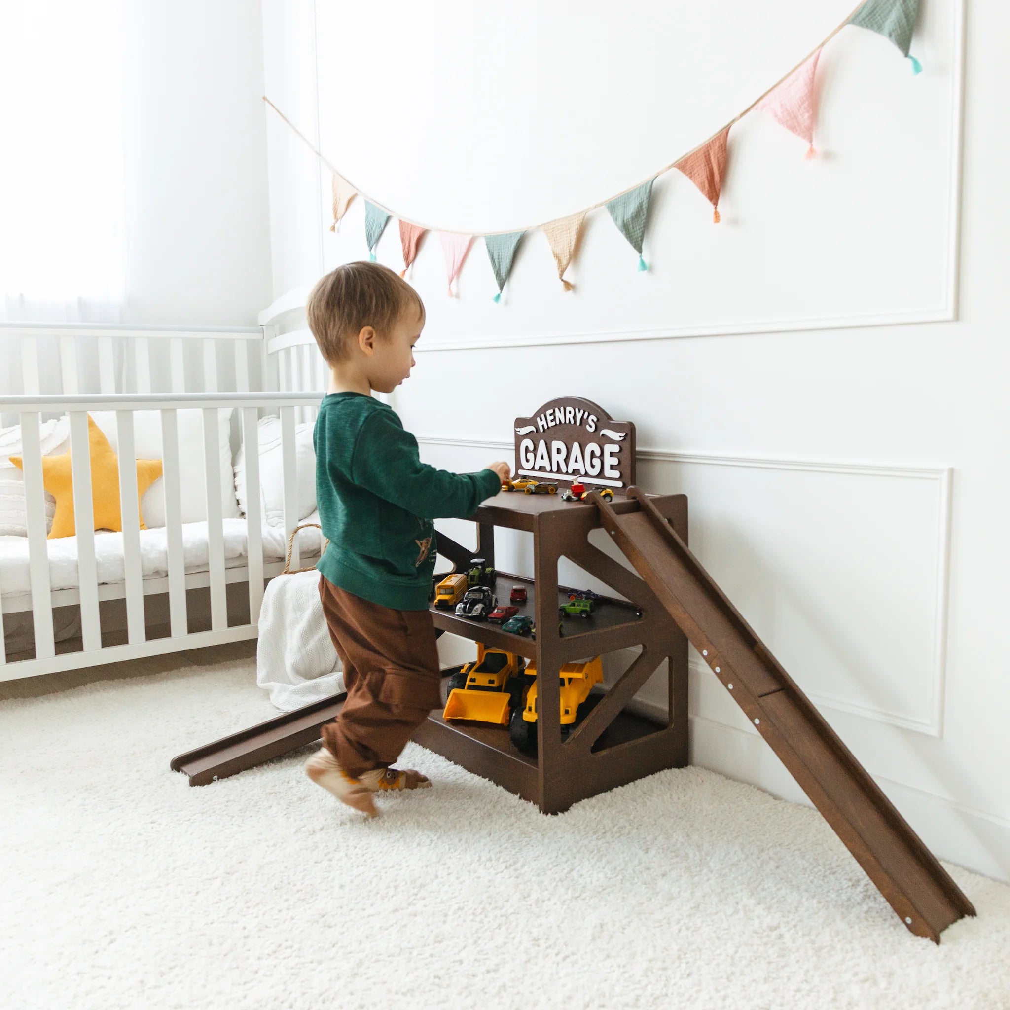 Toddler playing beside a dark wood personalized toy car garage named Henry's Garage