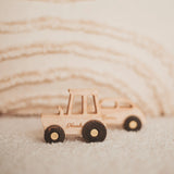 Natural wood toy cars on a cream blanket, including a pick-up truck engraved with a name
