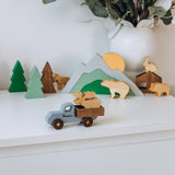 Wooden toy truck with a moose figure on a shelf with decorative mountains and trees.