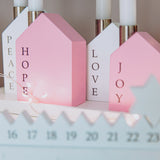 Decorative house-shaped candles with 'Hope', 'Love', and 'Joy' text on a shelf.