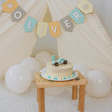 First birthday party setup with a personalized wooden car cake topper and an Oliver name banner