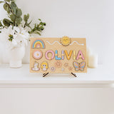 Wooden name board with decorative letters spelling 'OLIVIA', placed on a white surface with a plant in the background.