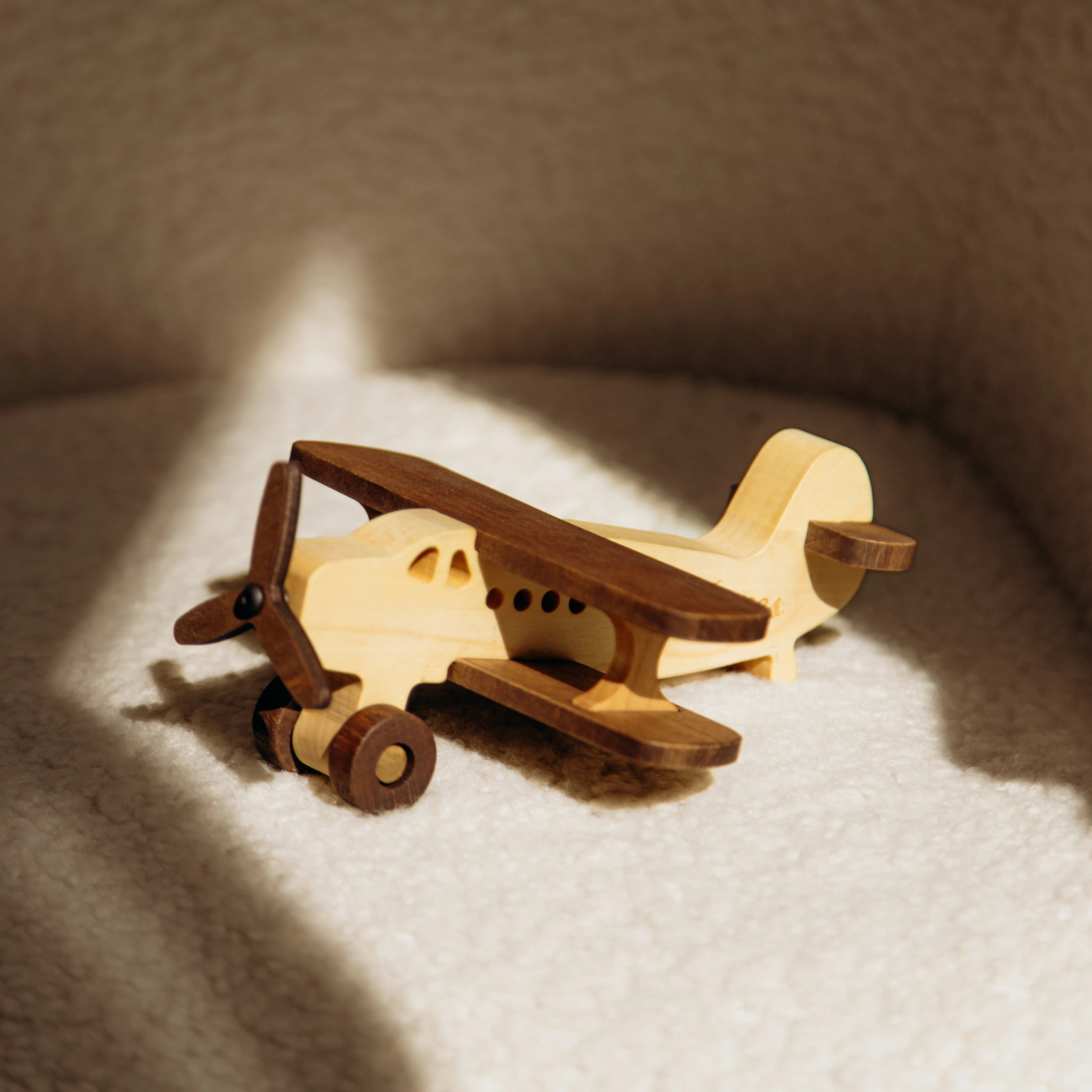 Natural wood biplane toy Model C on a beige knit blanket