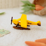 Yellow toy airplane with a custom printed name on a sandy surface.