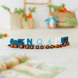 Wooden toy train with 'NOAH' wagon letters on a light surface with blurred background