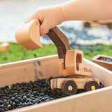 Wooden toy truck being played with by a child's hand over black beans.