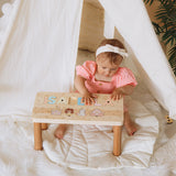 Baby sitting on a wooden stool with letters spelling 'ISABELLA' in a cozy indoor setting.