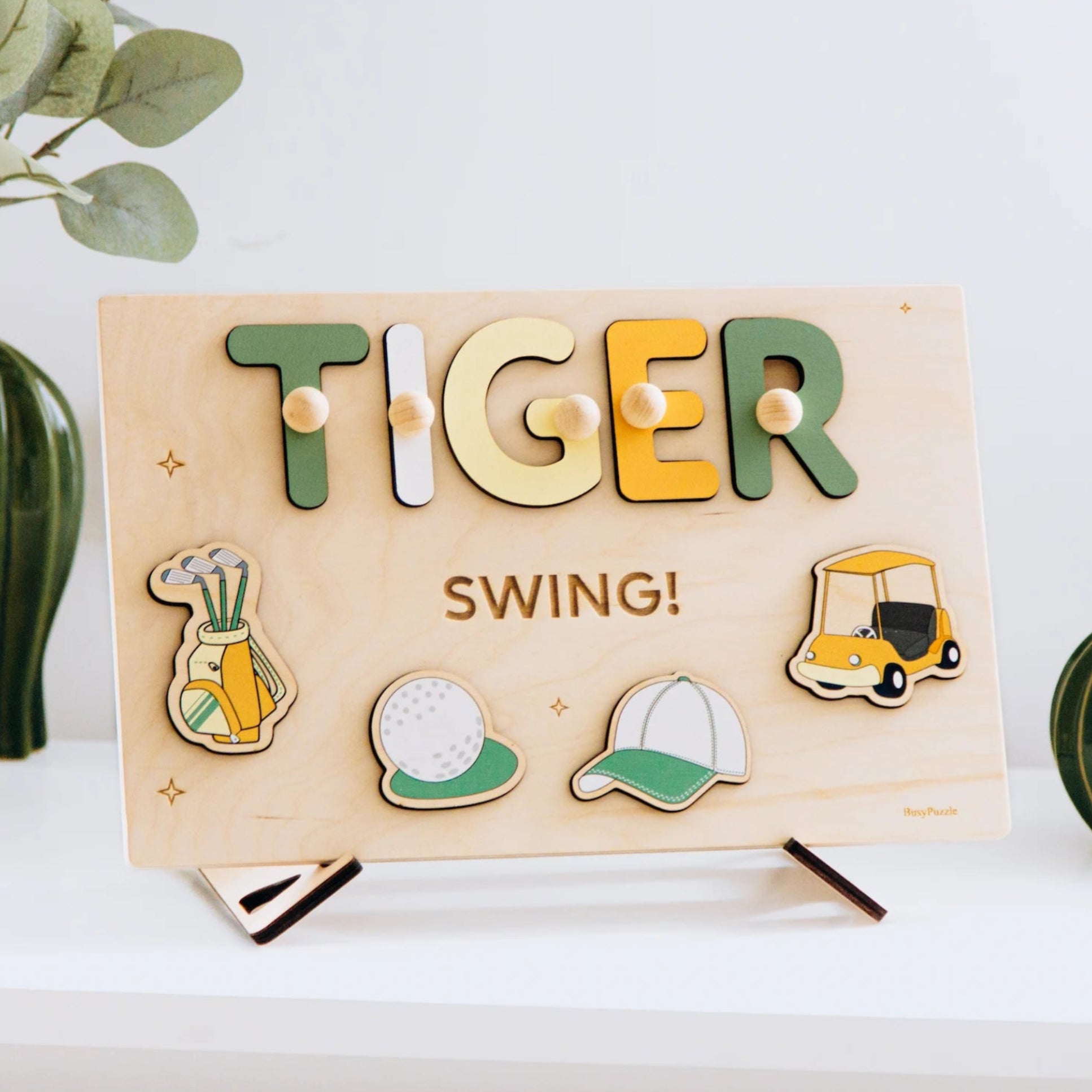 Wooden name puzzle spelling 'TIGER' on a stand, surrounded by plants.